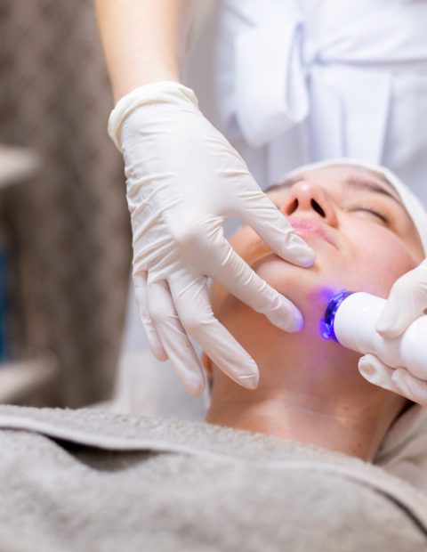 A young beautiful girl lies on the beautician's table and receives procedures with a professional apparatus for skin rejuvenation and moisturizing